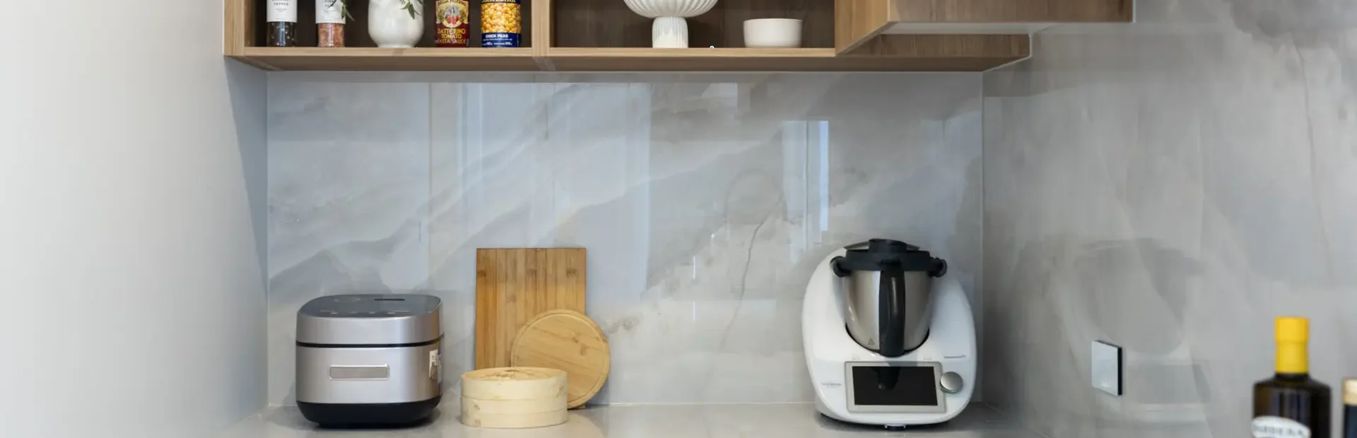 Butlers pantry featuring white kitchen cabinetry in shaker style with oak timber overheads and open shelving displaying styling items, thermomix on the benchtop with chopping boards and oils and black cooktop