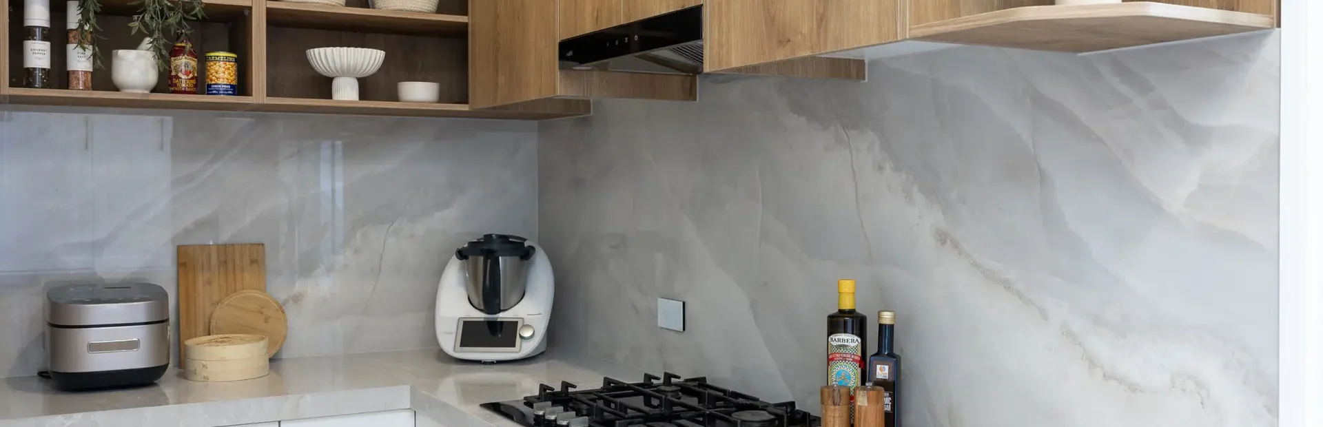 Butlers pantry featuring white kitchen cabinetry and oak overhead cabinets with oak open shelves displaying baskets and oils and salt and pepper shaker on stone benchtops