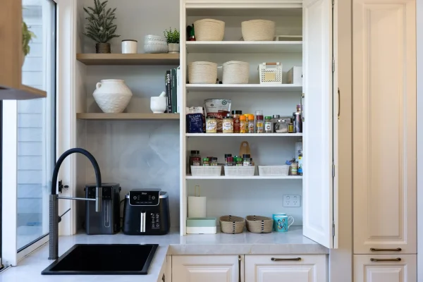 Butlers pantry featuring appliance cupboard in white shaker style cabinetry with pantry items, herbs and spices next to corner shelves in oak and black airfryer next to black sink and gooseneck tap