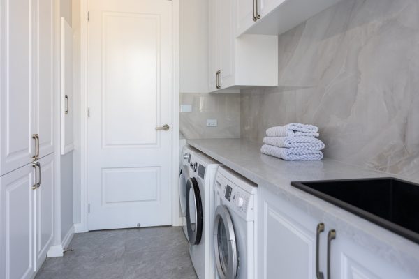 Laundry in galley style featuring white shaker style cabinetry in underbench and overheads on stone benchtops and splashbacks with washer dryer combination and black sink