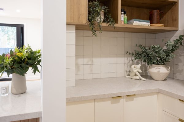 Butlers Pantry with white kitchen cabinetry, stone benchtops and white tiles featuring timber open shelves with styling items like cookbooks and plants with plant on benchtop next to lady ornament