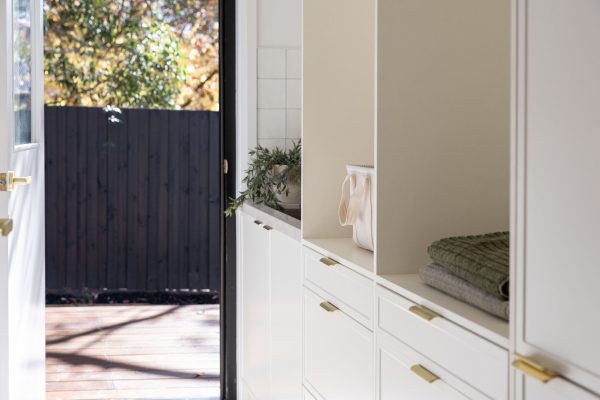 Laundry displaying white kitchen hampton cabinetry with brass handles and open shelves displaying green towels and white basket flowing to open door to external deck