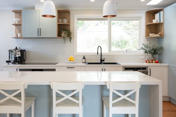 Green and white galley kitchen with white bench stools and large island bench with open timber shelving