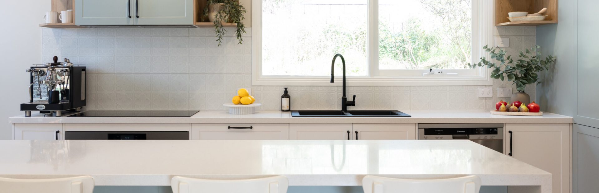 Green and white galley kitchen with white bench stools and large island bench with open timber shelving