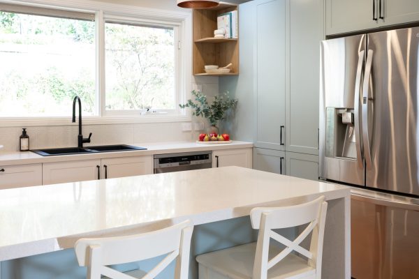 Green, timber and white kitchen with a large island bench with white benchstools and black sink and tap looking out the kitchen window