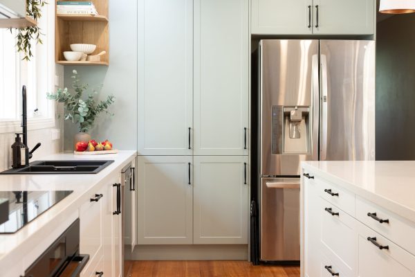 Green and white kitchen with black feature handles and open timber shelf with stainless still fridge
