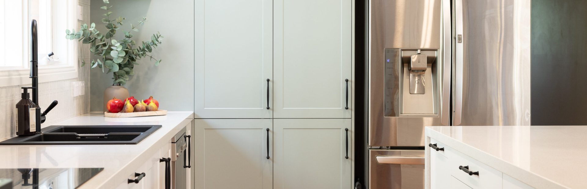 Green and white kitchen with black feature handles and open timber shelf with stainless still fridge