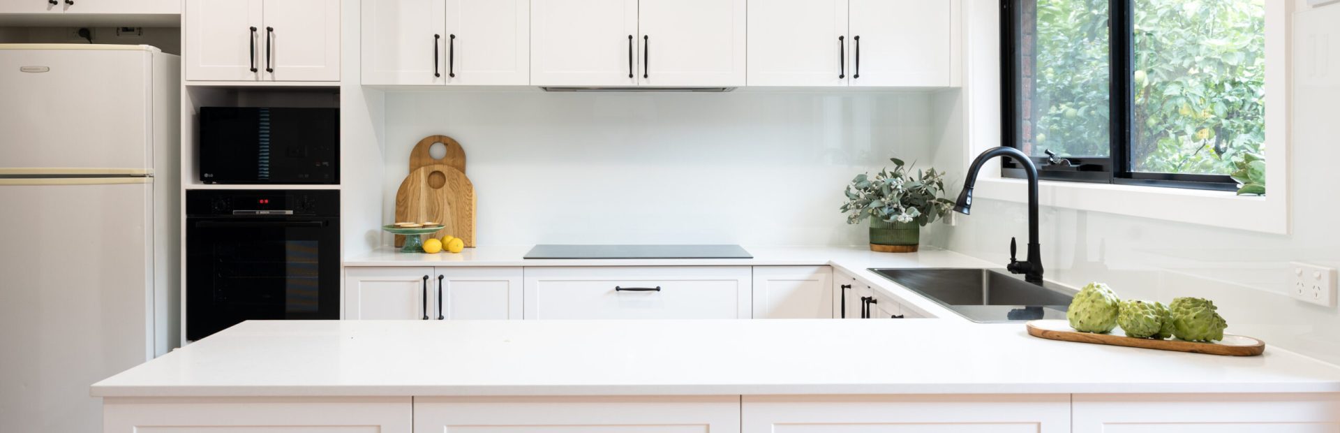 White shaker style cabinetry in this u shaped kitchen with black windows, black handles and black oven and microwave