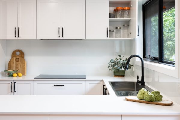 White shaker style kitchen with black handles and black sink and tap with black handles and plant on stone benchtops