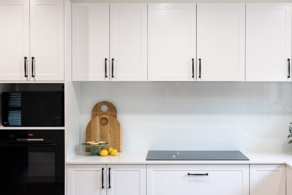 White shaker style kitchen cabinetry with black induction cooktop and timber chopping boards with green stand holding lemon tarts and lemons on stone benchtops
