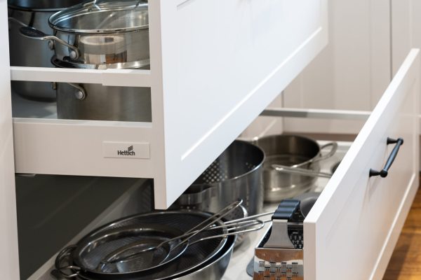 Two large white kitchen cabinetry pot drawers pulled out displayed with stainless steel pots and pans