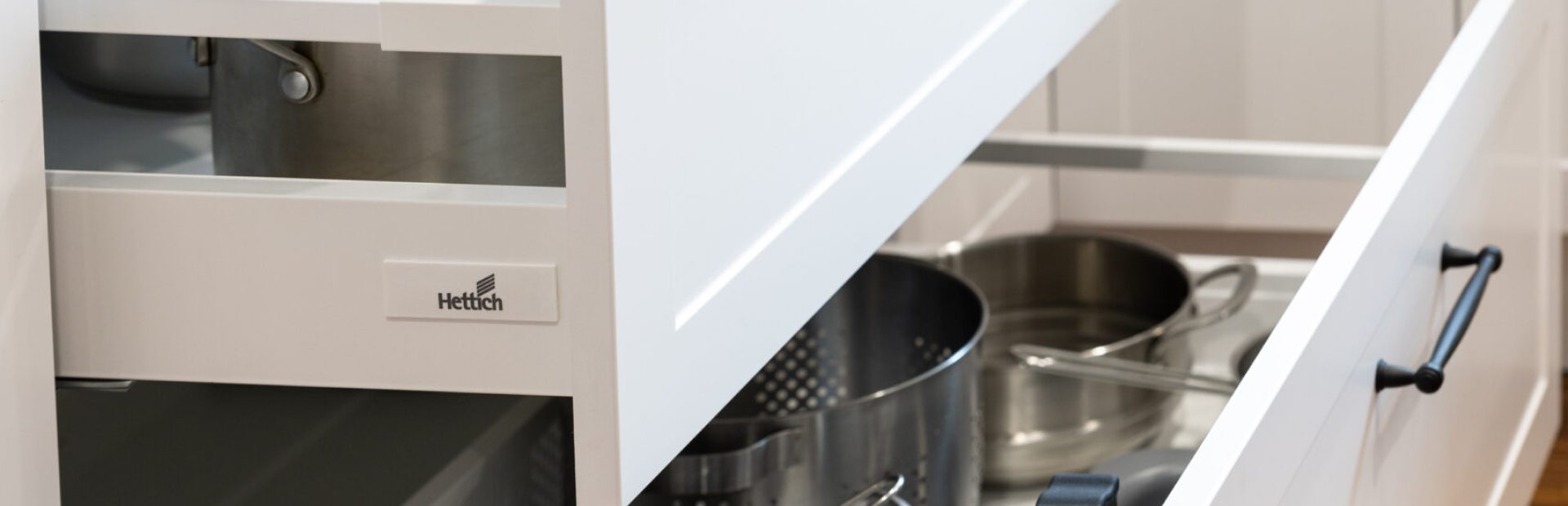 Two large white kitchen cabinetry pot drawers pulled out displayed with stainless steel pots and pans