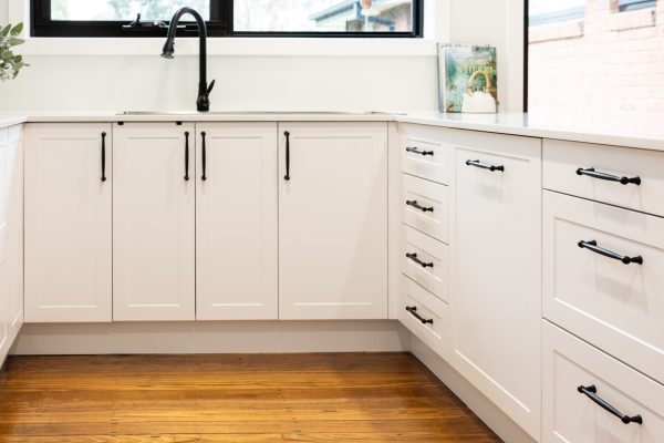U shaped white shaker style kitchen cabinetry with black decorative handles and black tap and sink with cookbooks and tea pot on stone benchtops