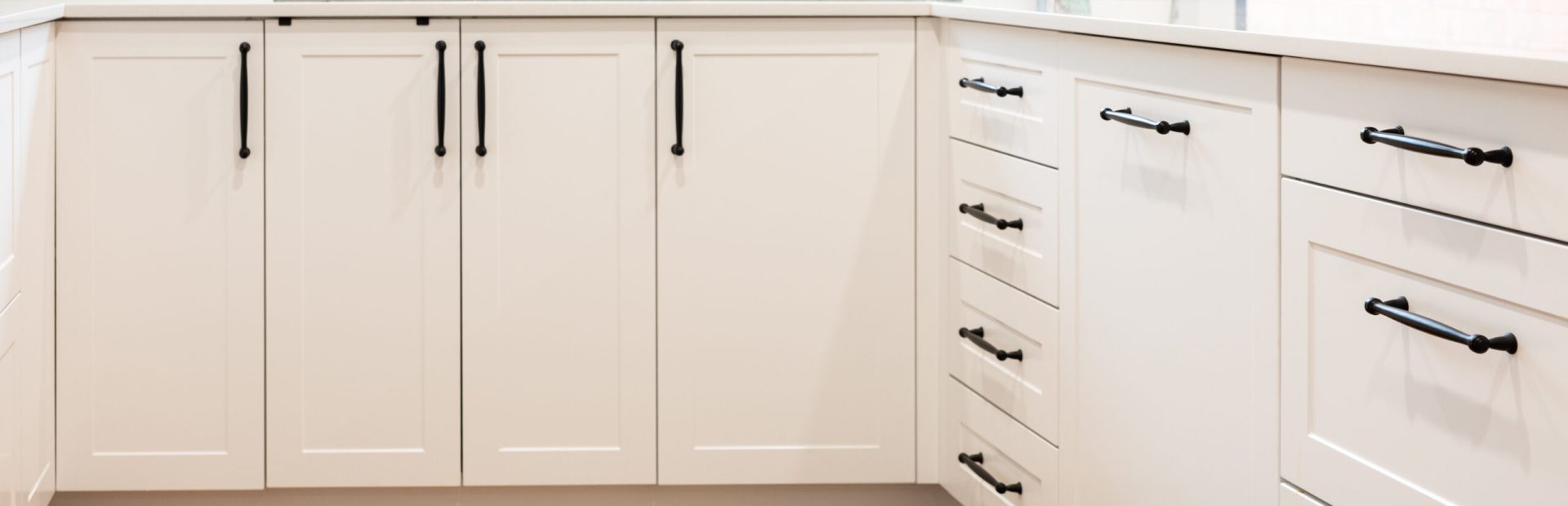 U shaped white shaker style kitchen cabinetry with black decorative handles and black tap and sink with cookbooks and tea pot on stone benchtops