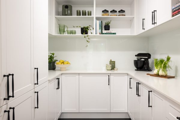 U shaped butlers pantry with white shaker style cabinetry with black handles and open shelves displaying green glasses, plant and styling items on stone benchtops