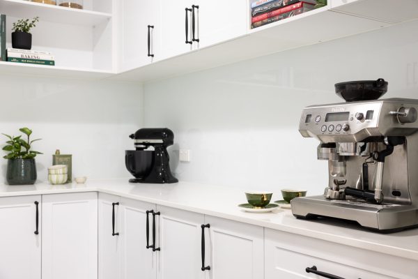 White shaker style kitchen cabinetry in a butlers pantry with black handles and black mix master and stainless steel coffee machine on stone benchtops