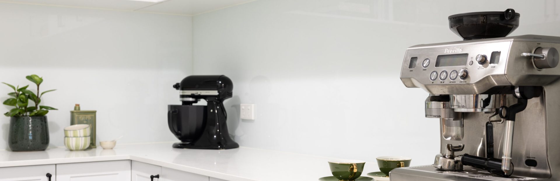 White shaker style kitchen cabinetry in a butlers pantry with black handles and black mix master and stainless steel coffee machine on stone benchtops