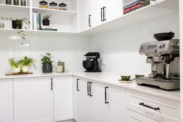 Butlers pantry displaying white shaker style kitchen cabinetry with black decorative handles and black mixmaster, potplant and cookbooks with plants in open white shelving