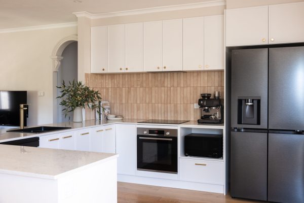 U shape kitchen with white hampton style kitchen cabinetry with brass handles, stone benchtops and black appliances against a pink tiled splashback