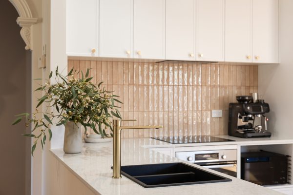 Kitchen displaying white hampton style with brass handles and vase with wattle on benchtop with brass tap and black sink