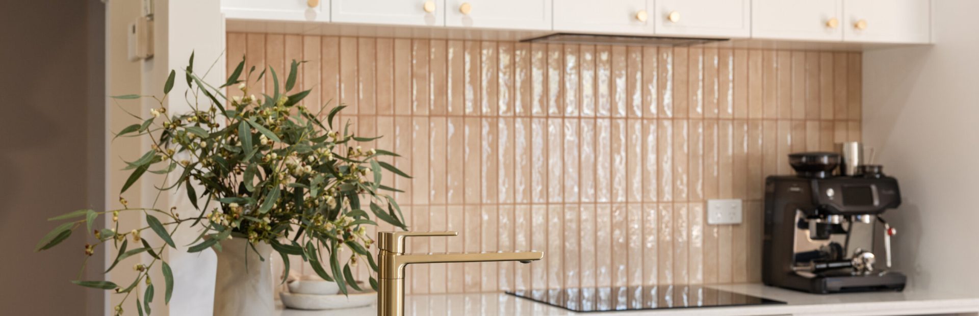 Kitchen displaying white hampton style with brass handles and vase with wattle on benchtop with brass tap and black sink