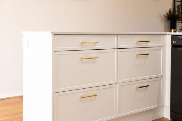 Bank of kitchen cabinets in white Hampton Style with brass horizontal handles and stone benchtops