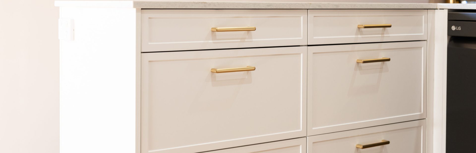Bank of kitchen cabinets in white Hampton Style with brass horizontal handles and stone benchtops