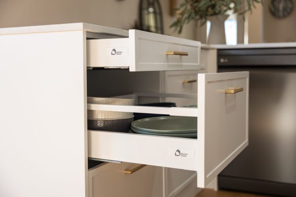 Kitchen drawers pull out displaying cutlery drawer and pot drawer in white kitchen with brass handles