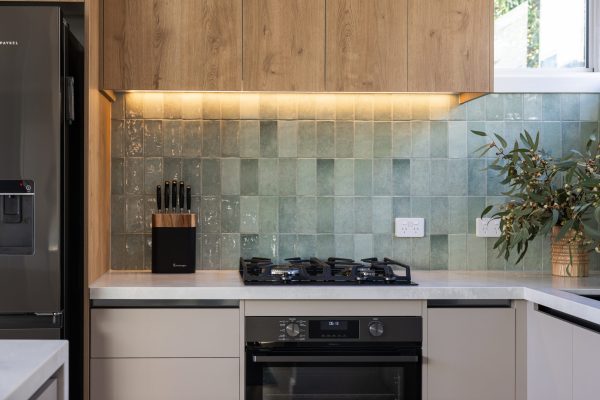 Oak laminate cabinetry with beige handle free cabinetry with black channel and striking green coloured splashback tiles