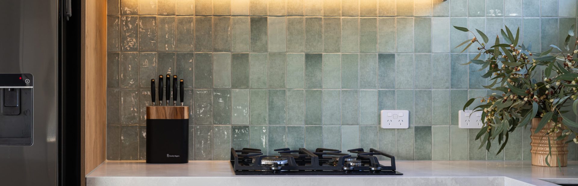 Oak laminate cabinetry with beige handle free cabinetry with black channel and striking green coloured splashback tiles