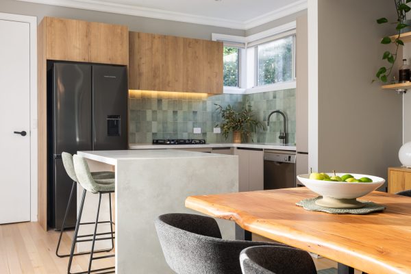 U shape kitchen with black friedge and sink and tap and oak overhead cabinetry with green tiled splashback and standalone island bench in stone