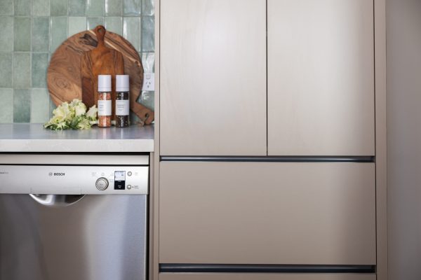 Kitchen pantry and pot drawer cabinetry in beige with black chanelling for handle free cabinetry styled with chopping boards and salt and pepper and folliage