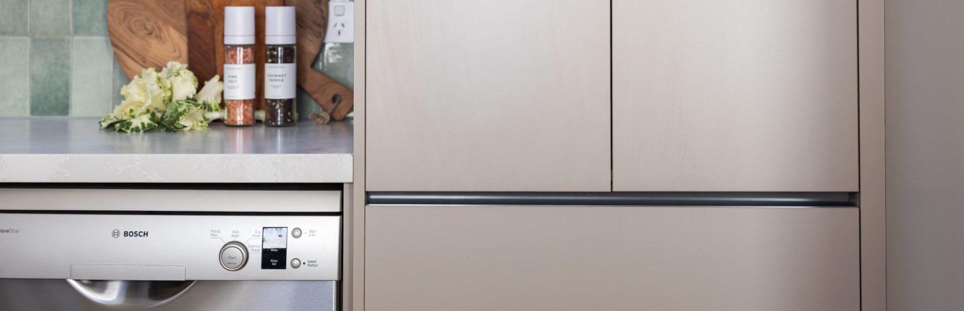 Kitchen pantry and pot drawer cabinetry in beige with black chanelling for handle free cabinetry styled with chopping boards and salt and pepper and folliage