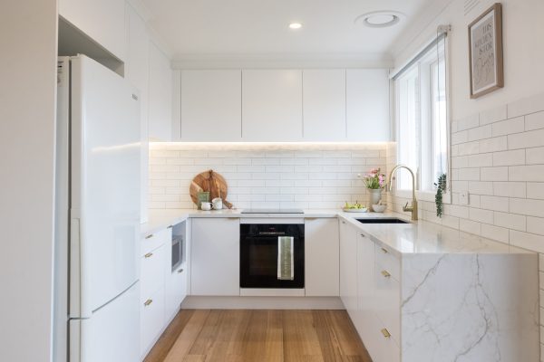 U shaped white kitchen with white and vein stone benchtop with wooden chopping boards and plants on kitchen benchtop for styling