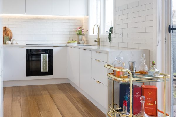 White kitchen with brass handles and tapware and black oven with brass drinks stand next to the kitchen