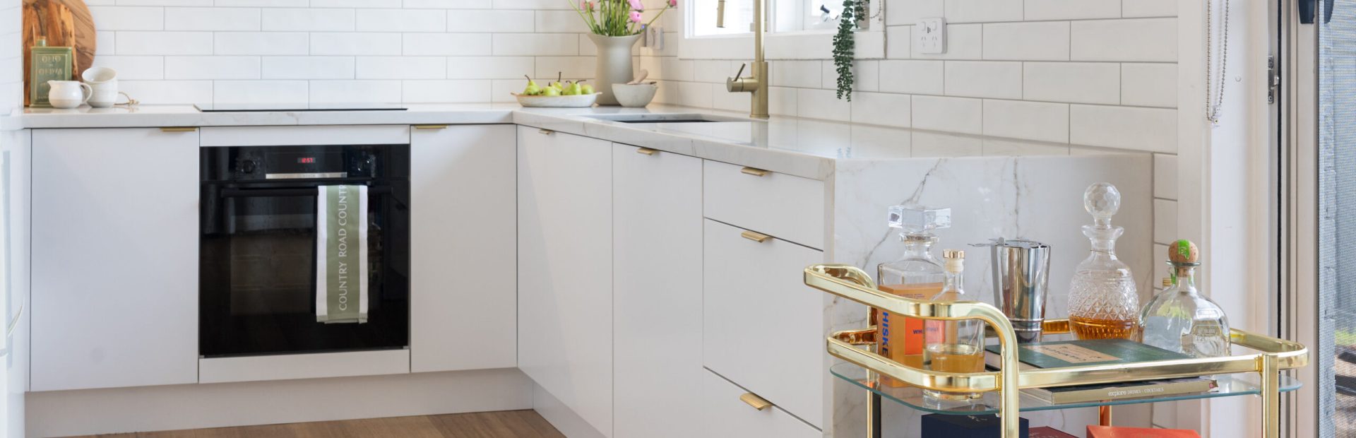 White kitchen with brass handles and tapware and black oven with brass drinks stand next to the kitchen