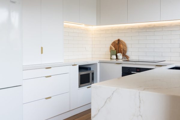 White kitchen displaying a microwave cabinet and appliance cabinet with brass handles and kitchen styling items on benchtop