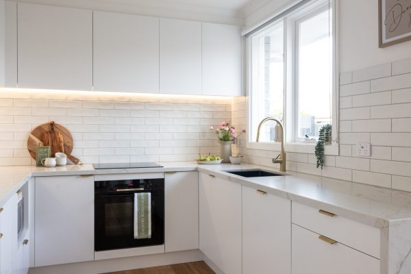 Kitchen displaying white cabinetry with stone veined benchtops and brass handles and tapware with plants for styling