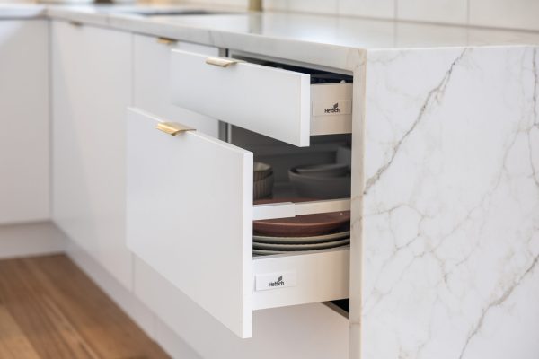 White kitchen displaying two pull out drawer sizes with brass handles and plates and bowls