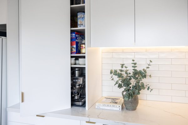 White kitchen pantry cabinetry with styling books and grey jug with green folliage on stone benchtop