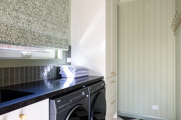 Laundry in galley style featuring tall hampton style cabinetry for storage with green walls, splashback and curtains