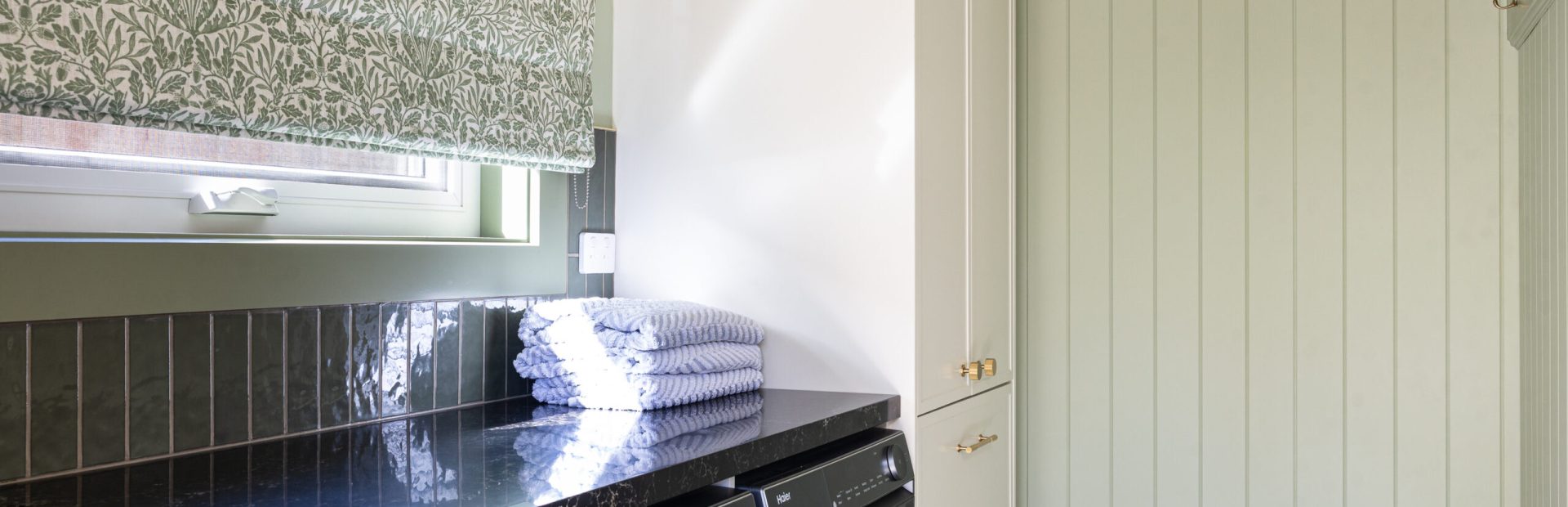 Laundry in galley style featuring tall hampton style cabinetry for storage with green walls, splashback and curtains