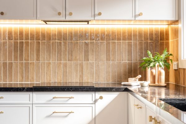 Parchment colour kitchen cabinetry in Hampton style with brass handles and brass styling items on a black benchtop