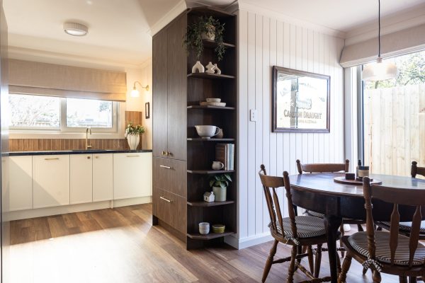Kitchen Renovation displaying sepia walnut coloured pantry with open shelving at end displaying styling items in a kitchen with parchment colour Hampton style and displayign round dark timber dining table