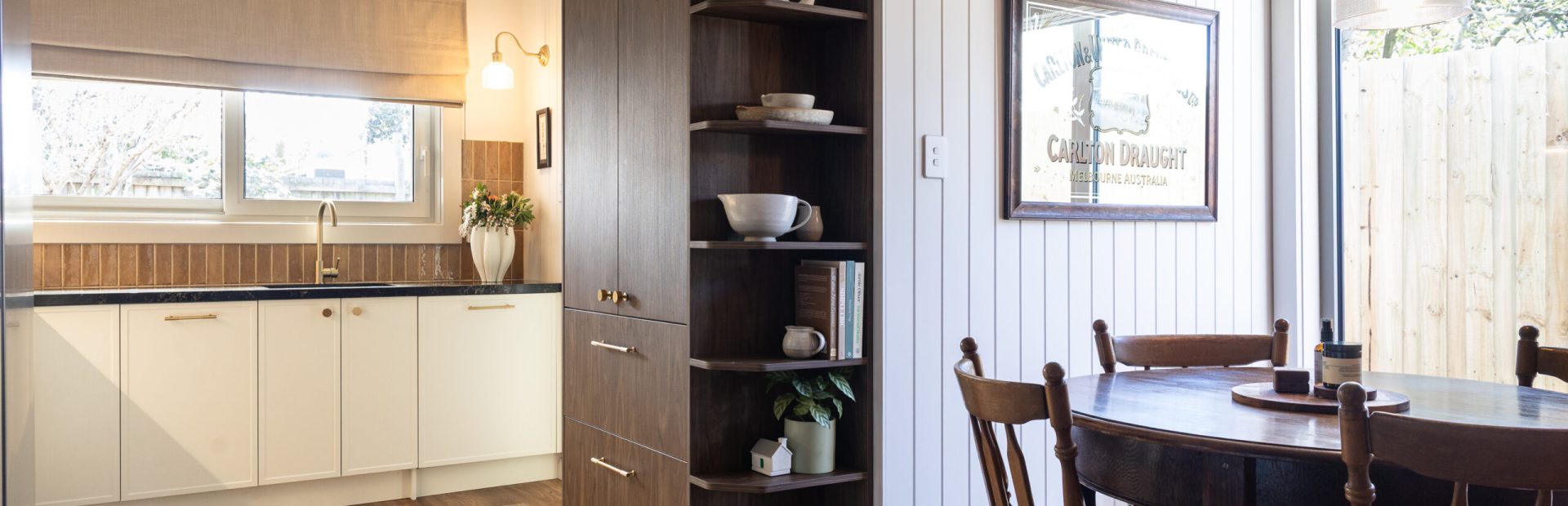 Kitchen Renovation displaying sepia walnut coloured pantry with open shelving at end displaying styling items in a kitchen with parchment colour Hampton style and displayign round dark timber dining table