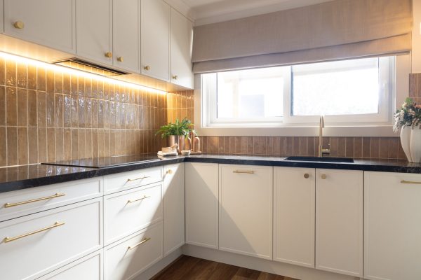Hampton style kitchen with parchment cabinetry and brass handles with black benchtops displaying brass pot plant and styling items on bench