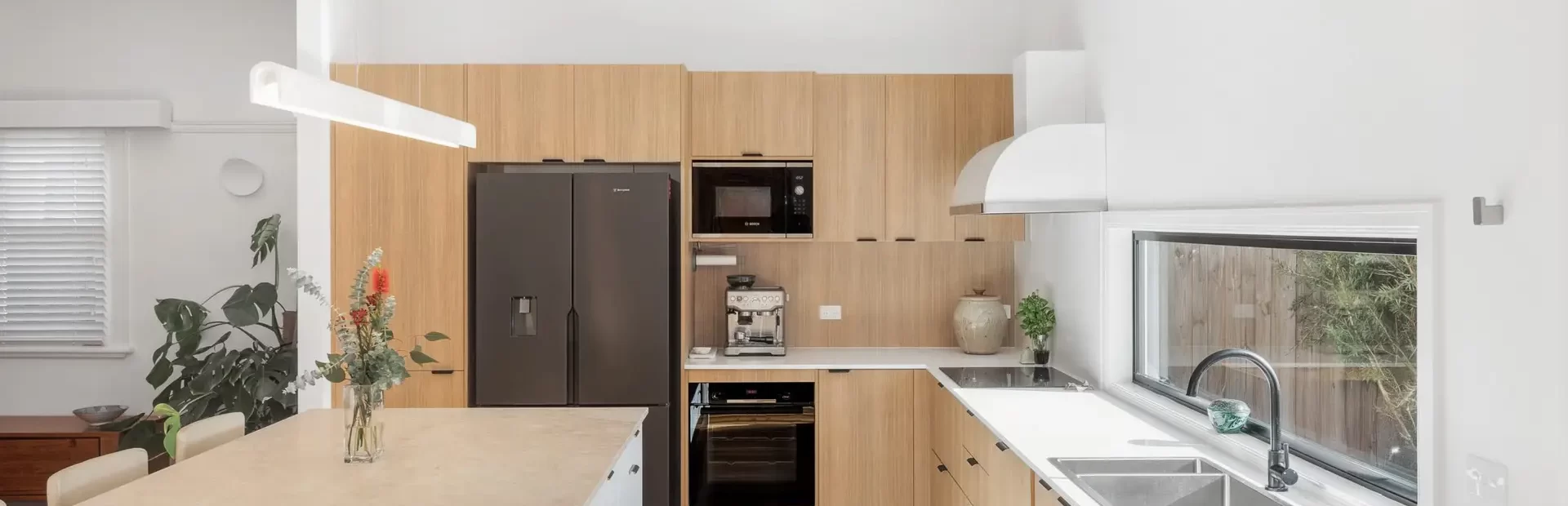 Galley kitchen featuring oak type laminate and white kitchen cabinetry with open plan window onto garden