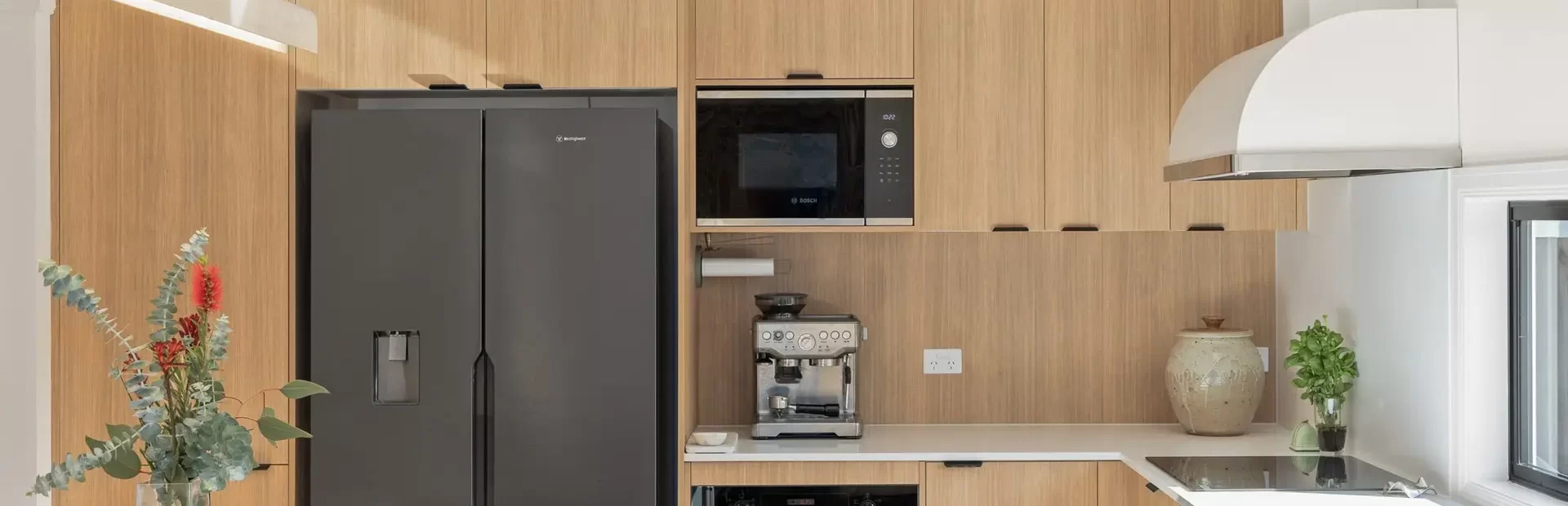 Oak Timber look kitchen cabinetry in us hspaed kitchen with black oven, microwave and fridge