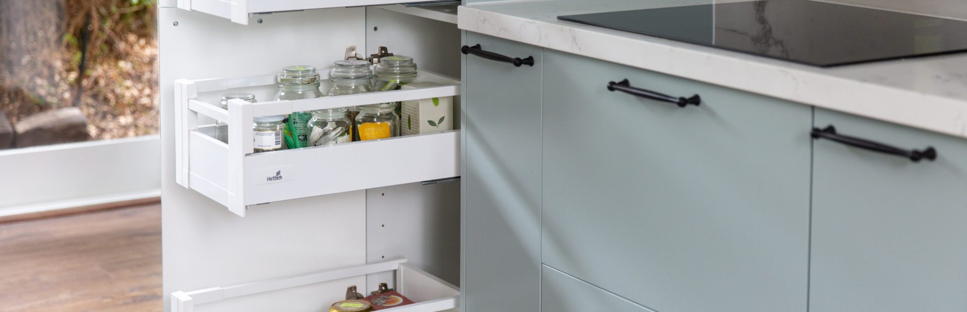Kitchen featuring pull out drawers in pantry with pantry items next to deep drawers in green colour cabinetry