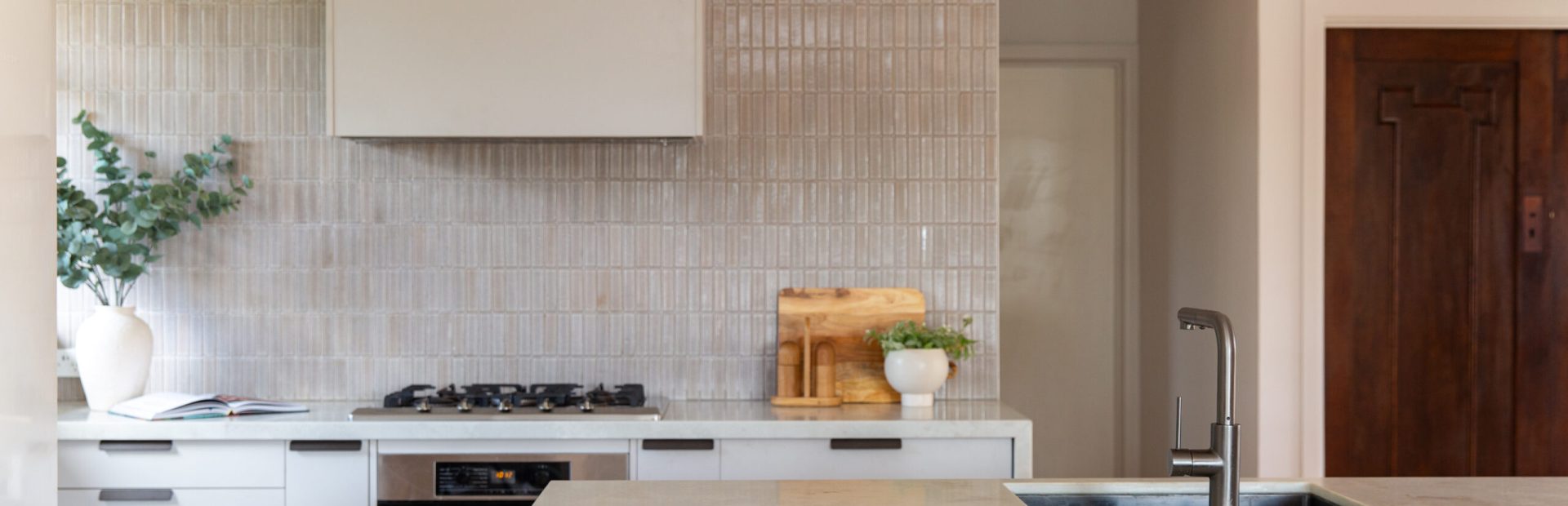 Oyster grey kitchen cabinetry in a galley kitchen featuring stainless stell oven and cooktop and plant and chopping board on bench